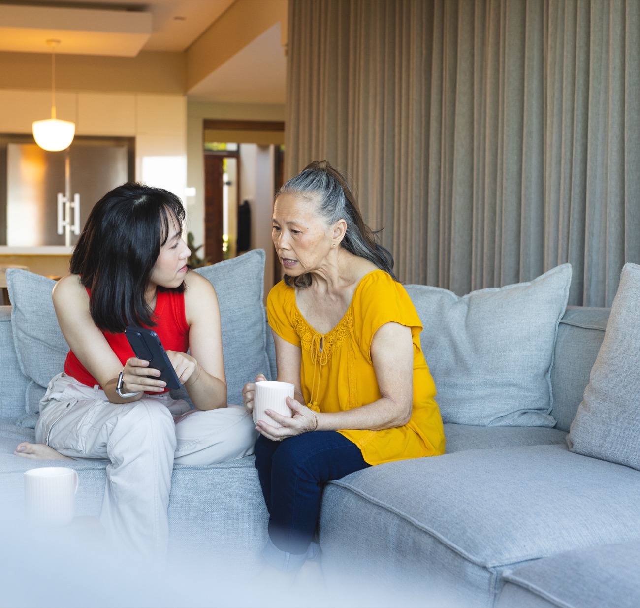 A caregiver and an older woman talking over a cup of tea on the sofa at home