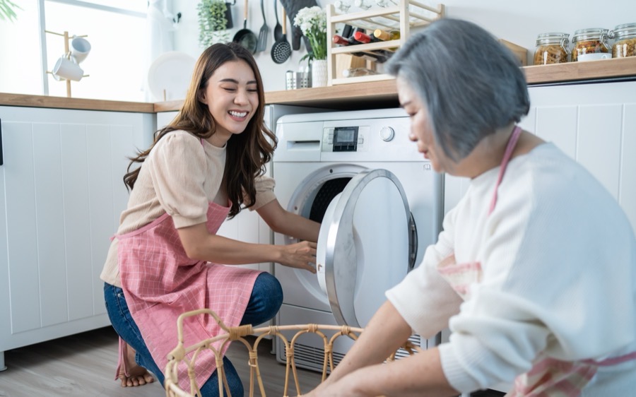 A caregiver helping an older woman load laundry into the washing machine