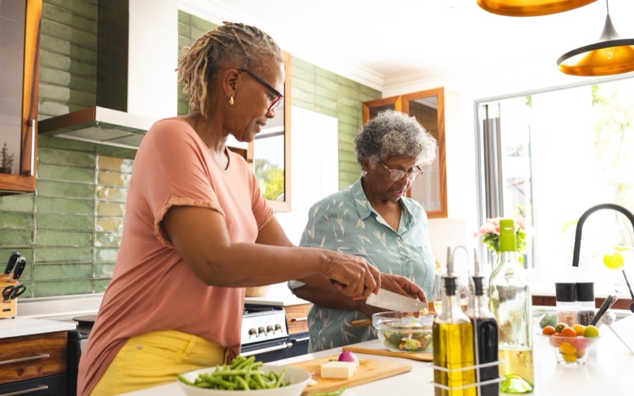 A caregiver and an older woman preparing a fresh salad together in a home kitchen
