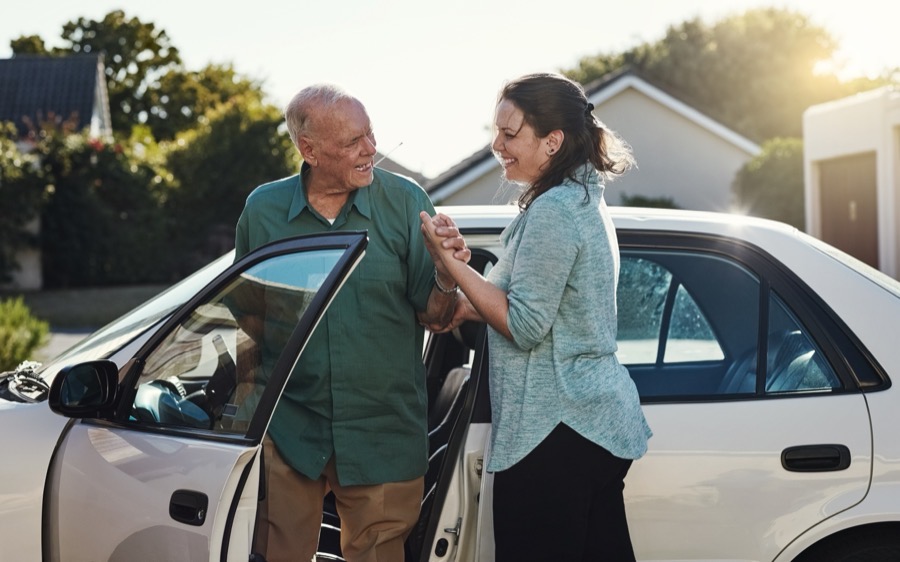 A caregiver helping an older man step out of the car outside his home