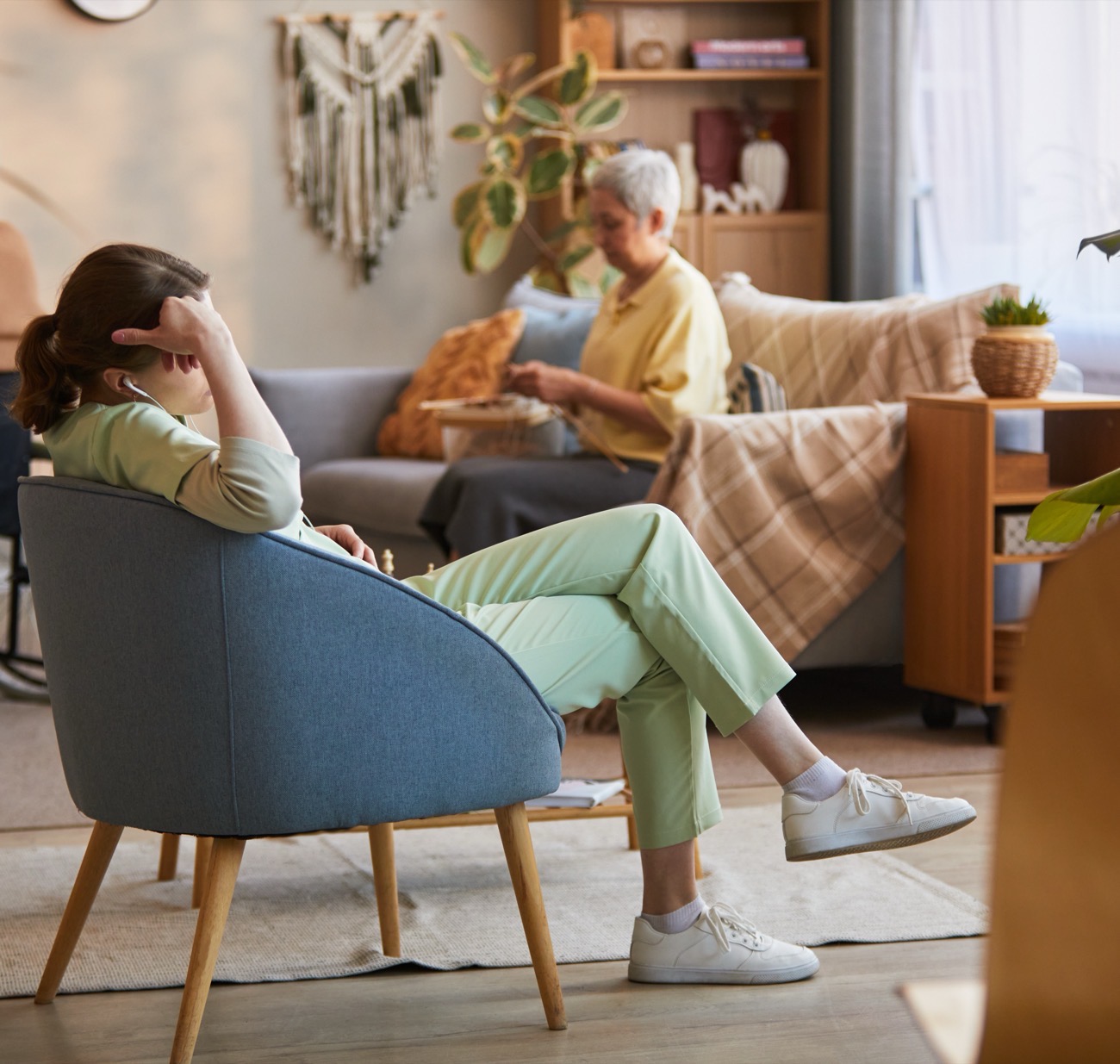 A family caregiver resting in an armchair while her relative sits nearby